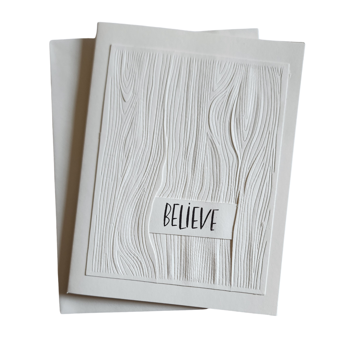 Ivory 5 × 7 handmade notecard with raised woodgrain embossing and BELIEVE sentiment, displayed with matching ivory envelope.